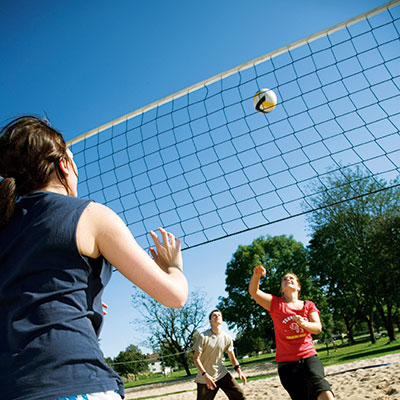 People play volleyball over a net in the middle and sand on the floor.